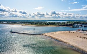 Luftbild der Travemünder Bucht mit Sandstrand, Mole und Segelboot. Das ATLANTIC Grand Hotel Travemünde liegt direkt am Meer.