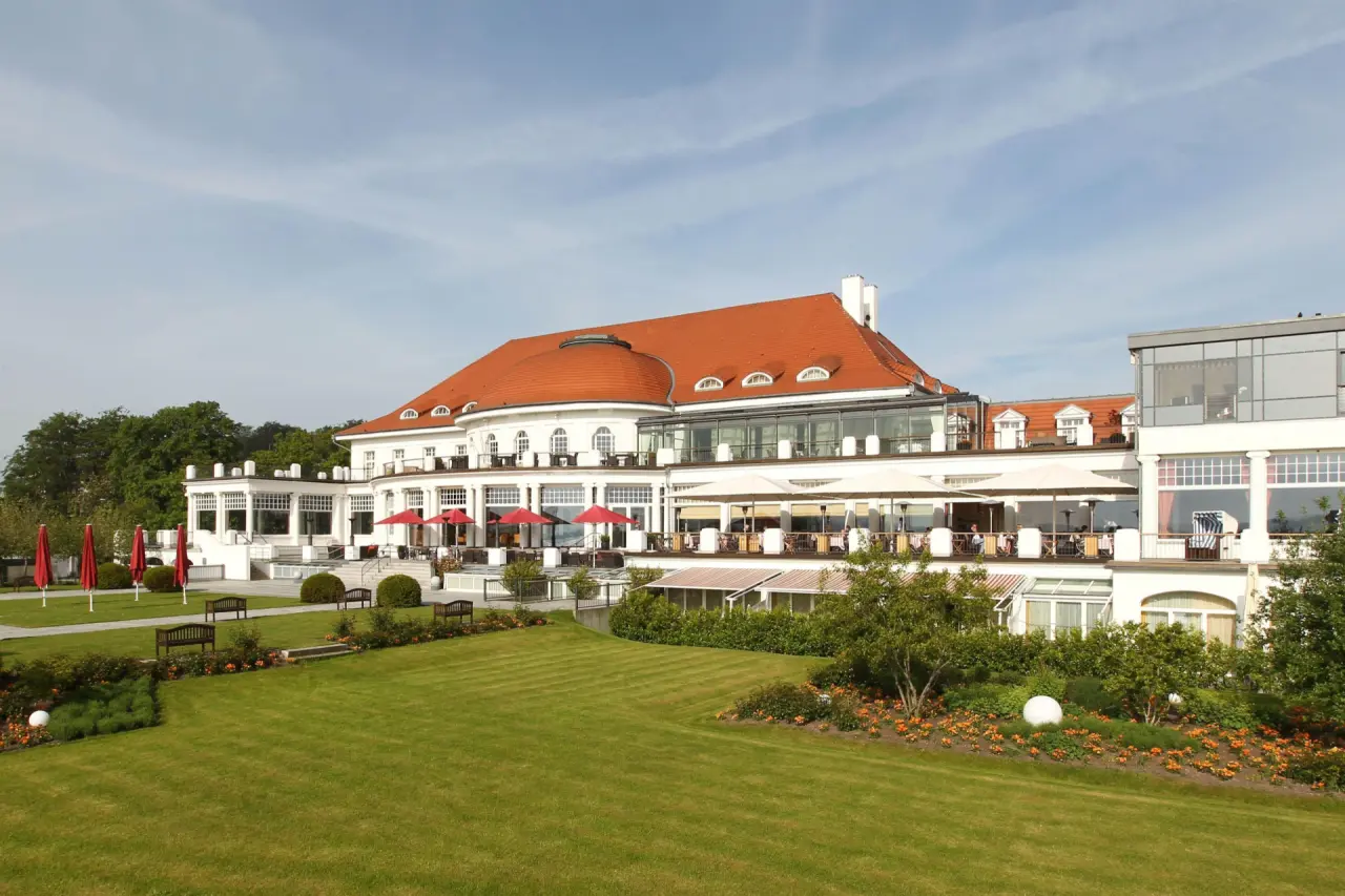 Elegante Aussenansicht des ATLANTIC Grand Hotel Travemünde mit rotem Dach, Terrassen und weitläufigem Garten.