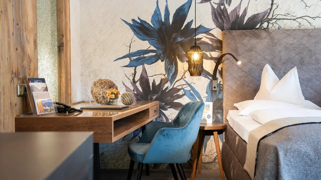 Modernes Hotelzimmer im Hotel Alpin Spa Tuxerhof mit Schreibtisch, blauem Sessel und floraler Wandgestaltung.