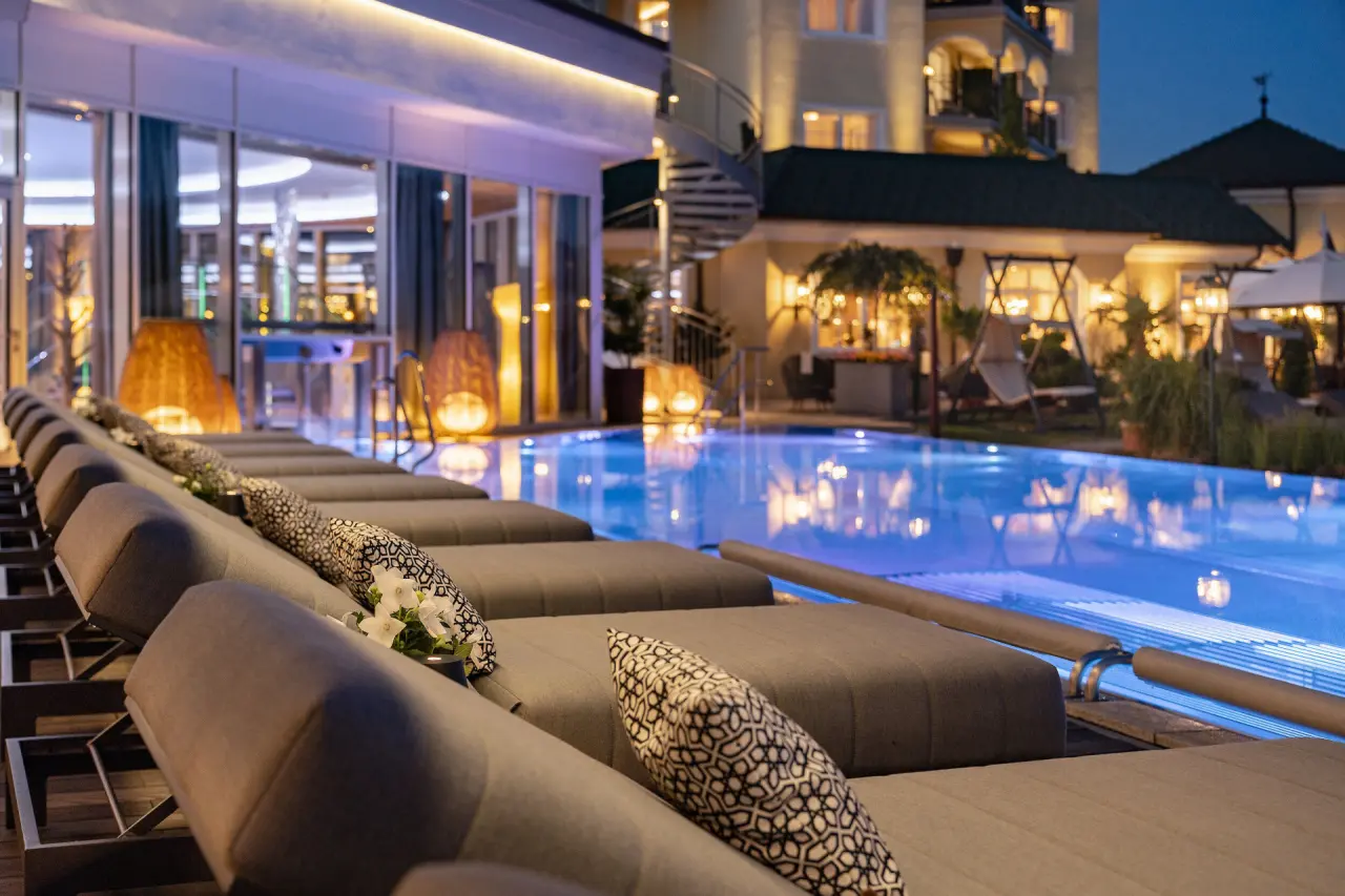Beleuchteter Aussenpool mit bequemen Liegen und Hotelgebäude bei Nacht im 5-Sterne Wellness- & Sporthotel Jagdhof.
