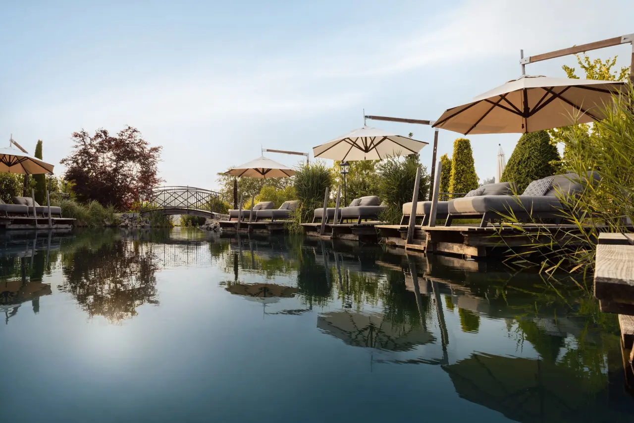 Naturschwimmteich mit luxuriösen Sonnenliegen und Schirmen im Gartenbereich des 5-Sterne Wellness- & Sporthotel Jagdhof.