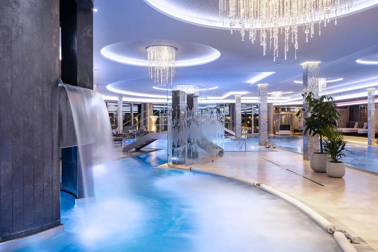 Luxuriöser Innenpool mit Wasserfall und eleganten Kronleuchtern im 5-Sterne Wellness- & Sporthotel Jagdhof.