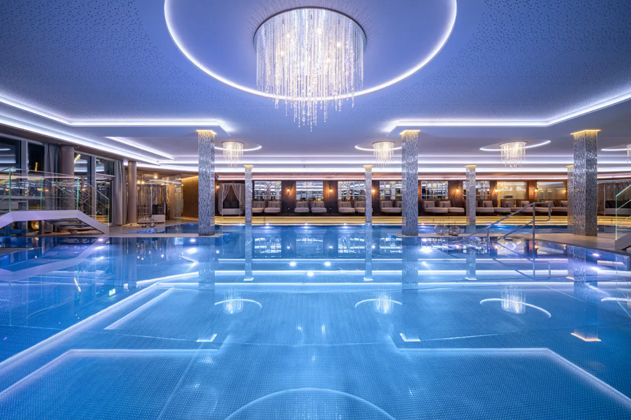 Luxuriöser Innenpool mit eleganten Kronleuchtern und Entspannungsliegen im 5-Sterne Wellnesshotel Jagdhof.