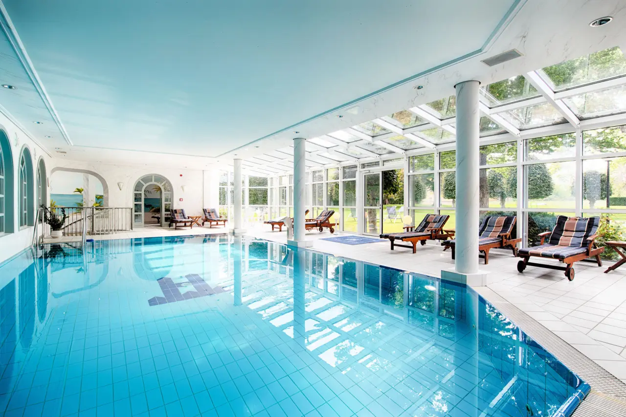 Helles Hallenbad mit grossen Fenstern und Blick in den Garten im Hotel Villa Heine. Entspannung am Pool.