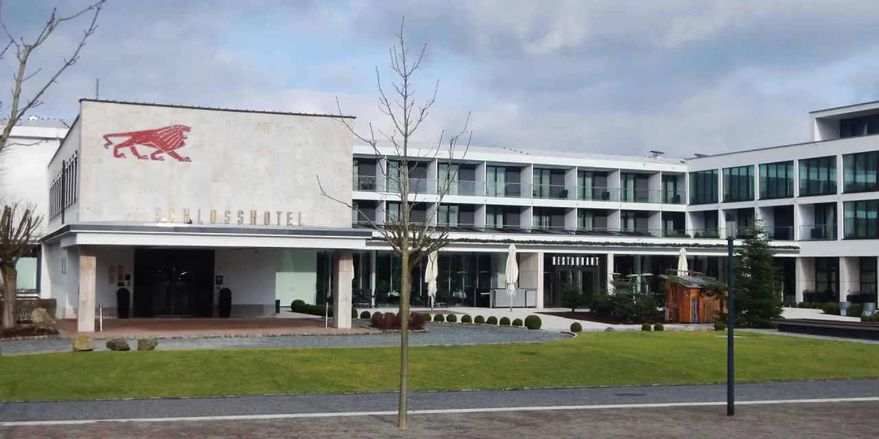 Moderne Aussenansicht des Schlosshotel Bad Wilhelmshöhe mit Eingang und Restaurantbereich unter bewölktem Himmel.