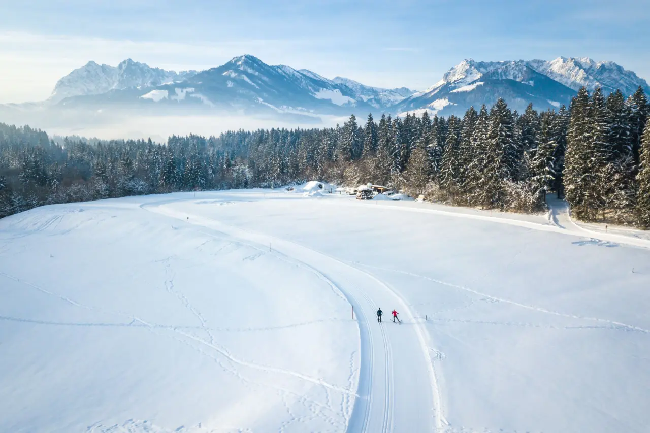 Langläufer auf Loipe im verschneiten Alpenpanorama mit Wald und Bergen, nahe Hotel Alpina.