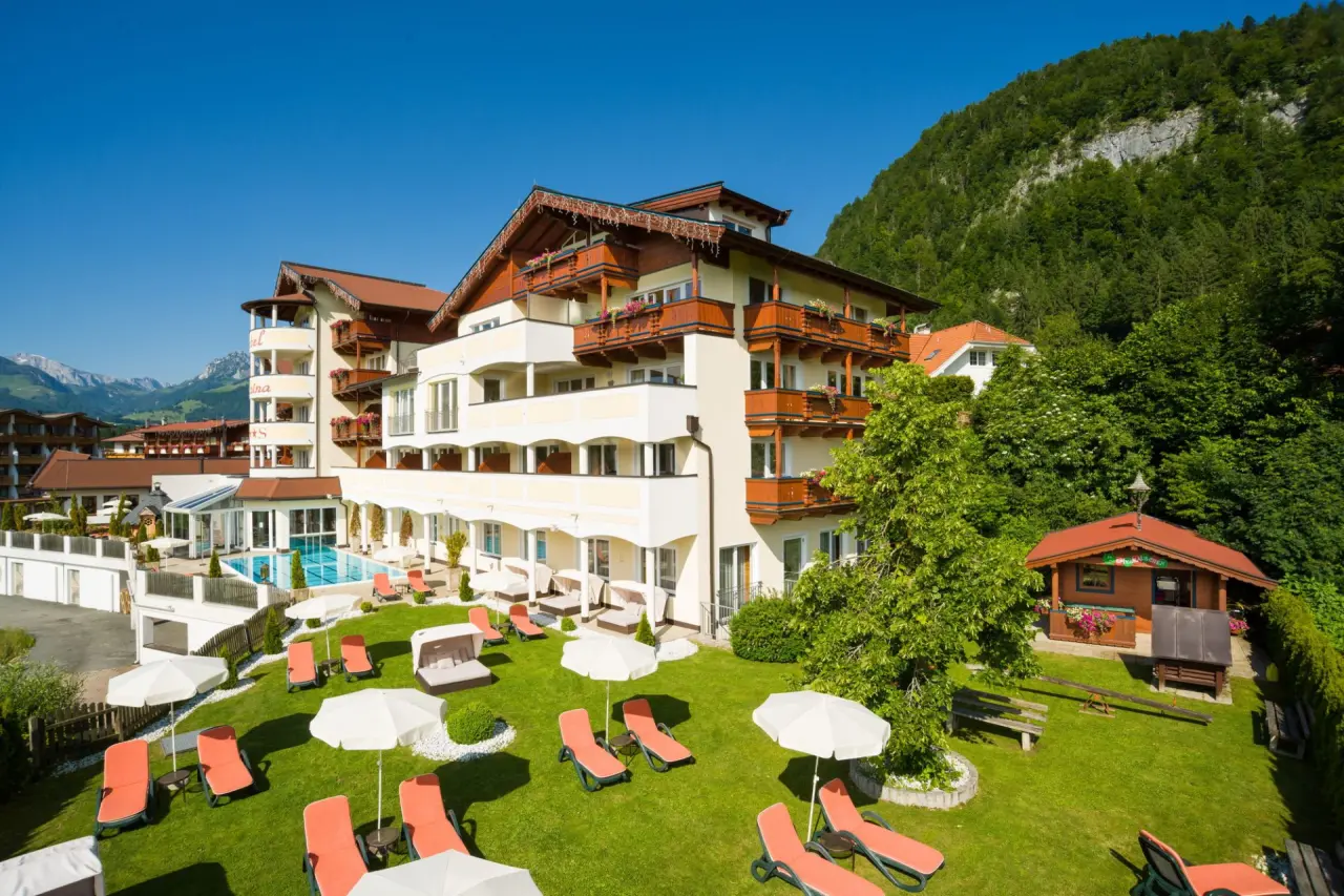 Aussenansicht des Hotel Alpina mit sonnigem Garten, Aussenpool und beeindruckendem Alpenpanorama.