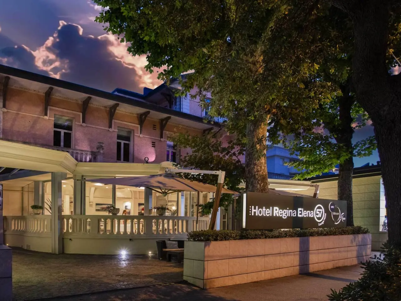 Hotel Regina Elena 57 in Rimini – Beleuchtete Außenansicht mit Hotel-Schild bei Dämmerung | Wellnesshotel Adriaküste