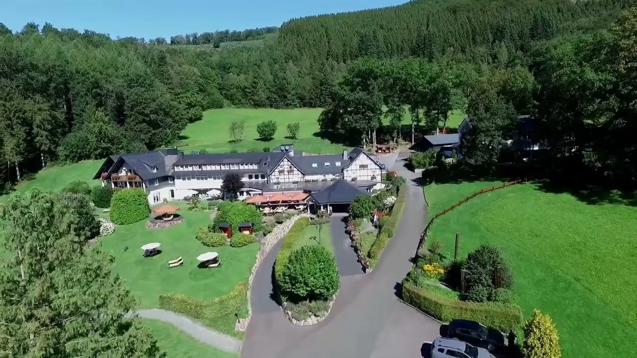 Luftaufnahme des Hotel Haus Hilmeke inmitten grüner Wälder und Wiesen, mit Zufahrt und Gartenbereich.