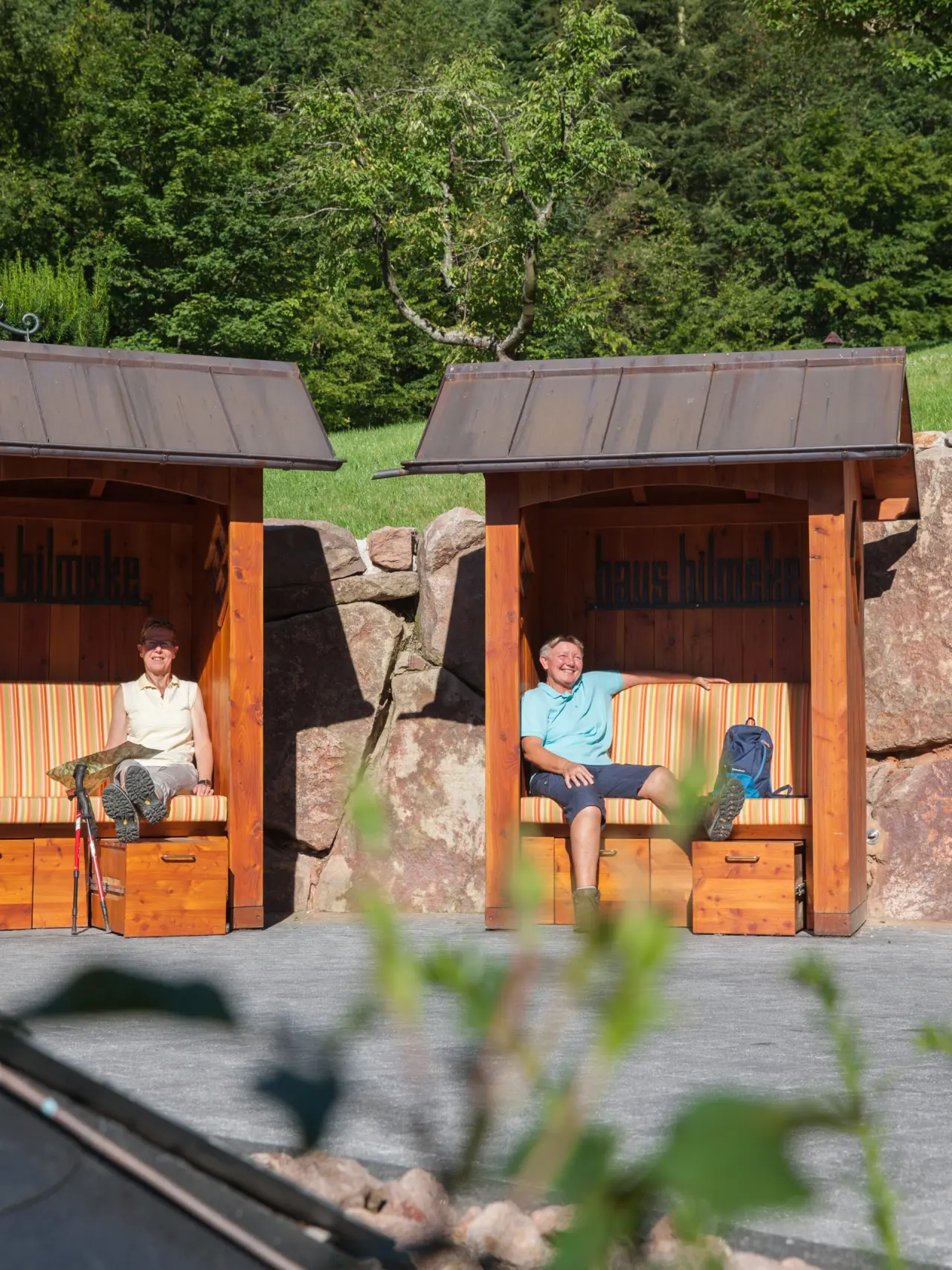 Gäste entspannen in gemütlichen Holz-Sitznischen im grünen Garten des Hotel Haus Hilmeke nach einer Wanderung.
