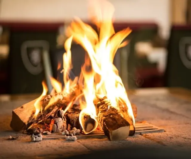 Gemütliche Feuerstelle mit lodernden Flammen und Holzscheiten im Sporthotel Royer Schladming für entspannte Abende.