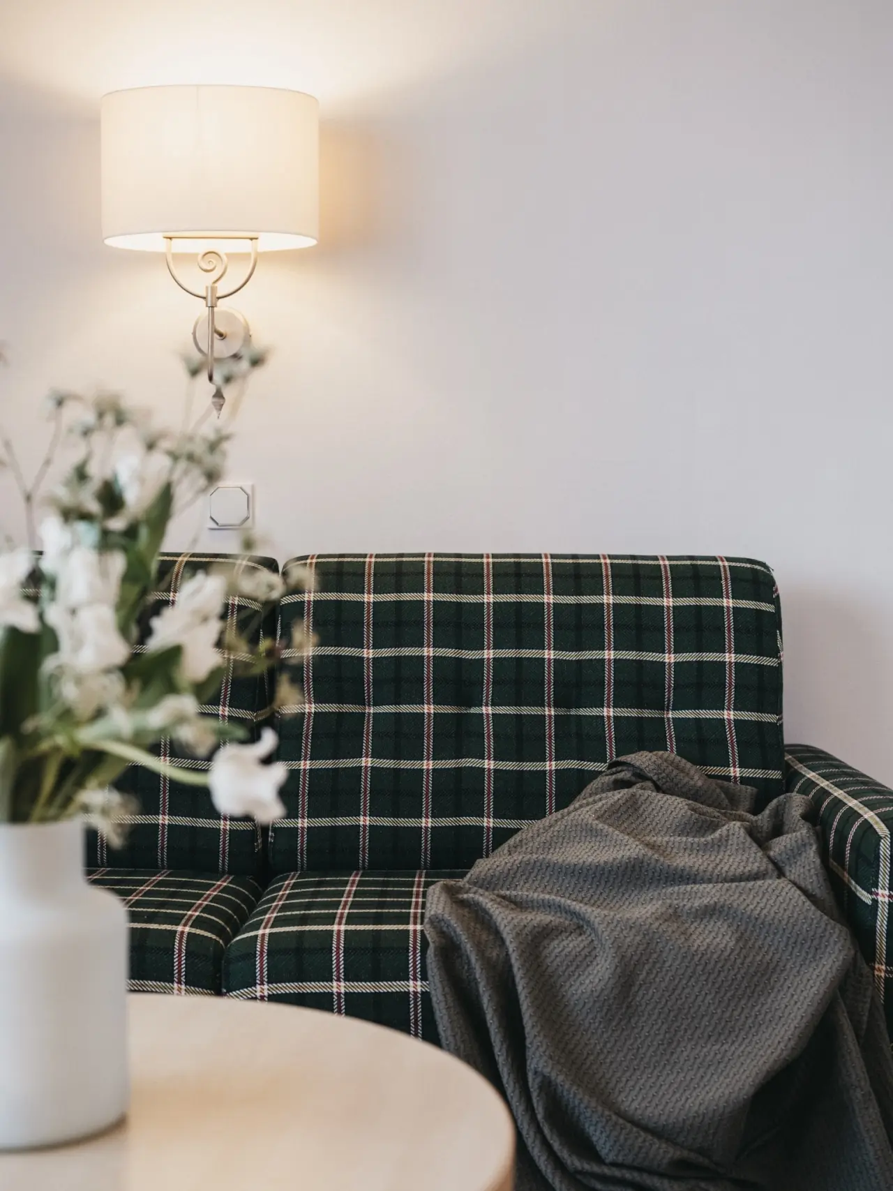 Gemütliches Sofa mit Schottenmuster und Decke unter einer Wandlampe im Sporthotel Royer Schladming.