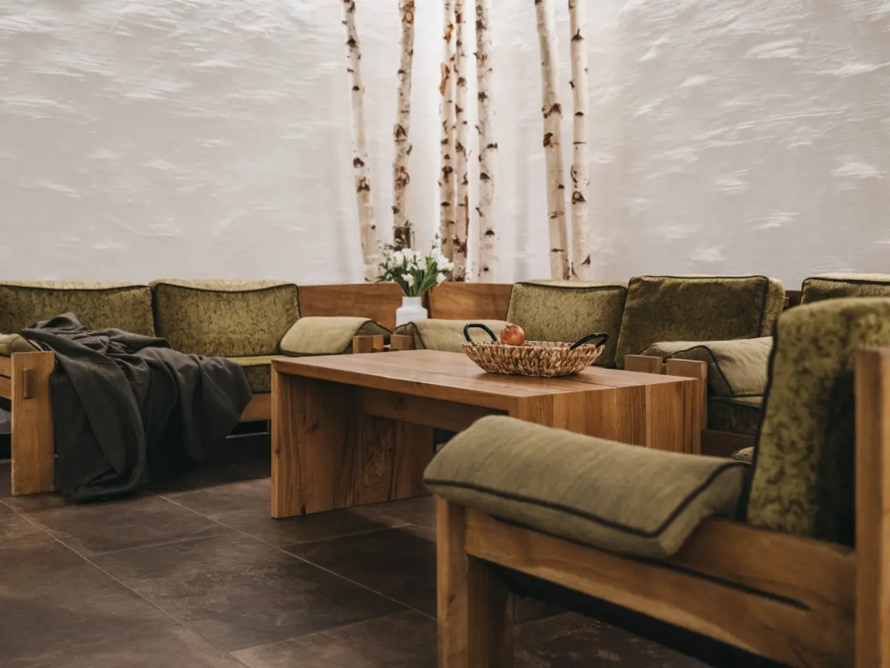 Gemütlicher Ruhebereich mit Holzbänken, grünen Kissen und Birkenstämmen im Wellnessbereich des Sporthotels Royer Schladming.