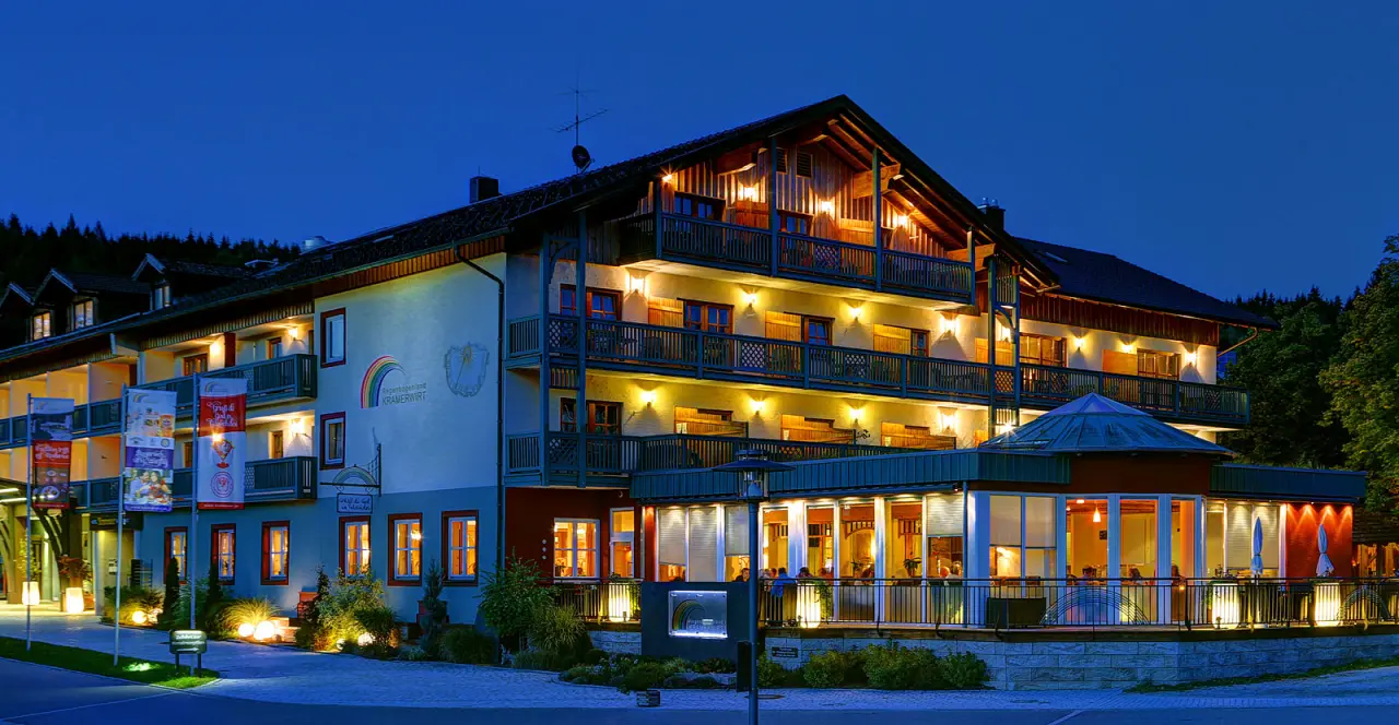 Abendansicht des traditionellen Hotel Zum Kramerwirt mit beleuchteten Balkonen und Restaurantbereich unter blauem Himmel.