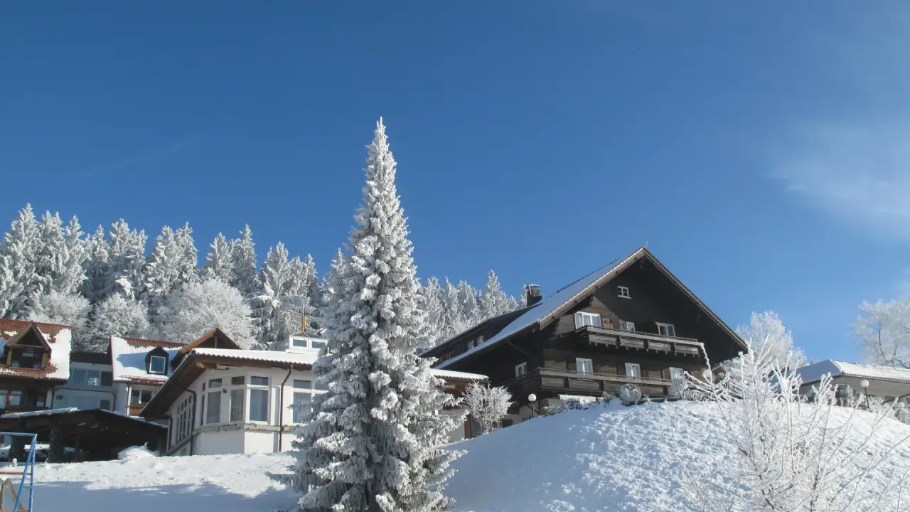 Berghotel Jägerhof im Winter, umgeben von tief verschneiten Tannen unter strahlend blauem Himmel. Perfekt für Winterurlaub.