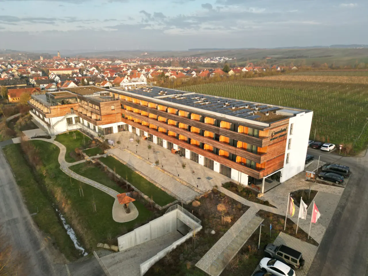 Luftaufnahme des sonnenhotel WEINGUT RÖMMERTH mit moderner Holzfassade, umgeben von Weinbergen und einem Dorf.