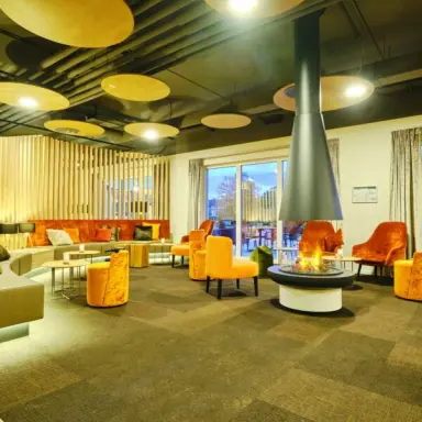 Gemütliche Hotellounge mit modernem Kamin und bequemen orangefarbenen Sesseln im sonnenhotel WEINGUT RÖMMERTH.