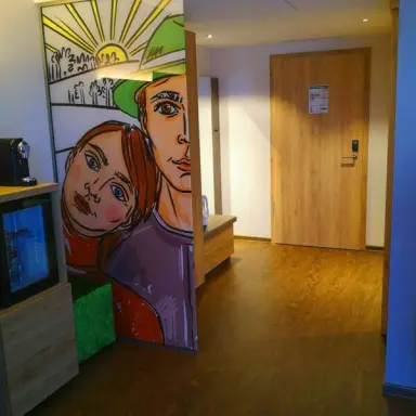 Eingangsbereich eines Hotelzimmers im sonnenhotel WEINGUT RÖMMERTH mit moderner Wandkunst und Minibar.