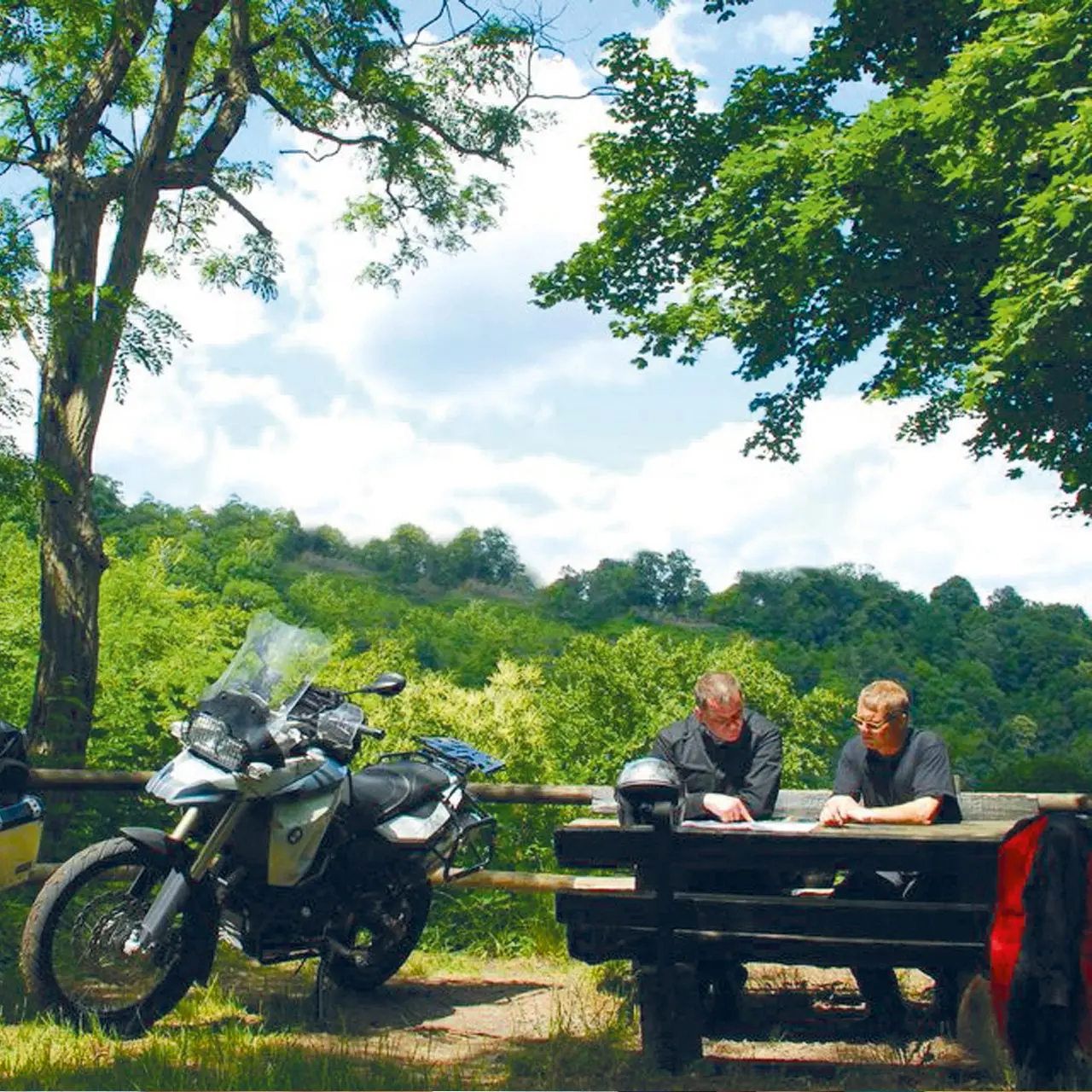 Zwei Motorradfahrer studieren eine Karte an einem Picknicktisch im Grünen, nahe dem Parkhotel Zum Stern.