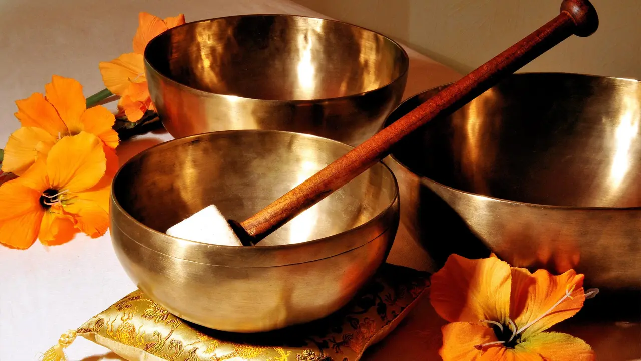 Drei goldene Klangschalen mit Klöppel und orangefarbenen Blüten für Wellness im Parkhotel Zum Stern.