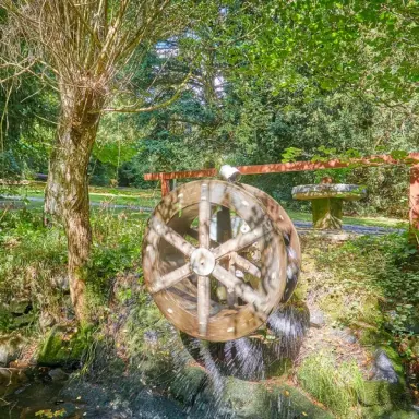 Historisches Wasserrad im idyllischen Garten des Parkhotel Zum Stern, umgeben von üppigem Grün und einem Bach.