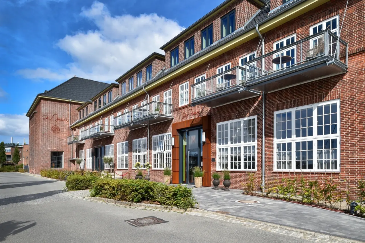 Aussenansicht des Hotels Das James mit roter Backsteinfassade, weissen Fenstern und Balkonen unter blauem Himmel.