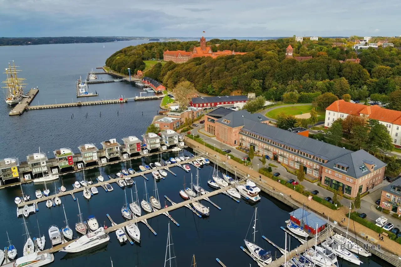 Luftaufnahme des Hotels Das James an der Flensburger Förde mit Yachthafen, historischen Gebäuden und grüner Umgebung.