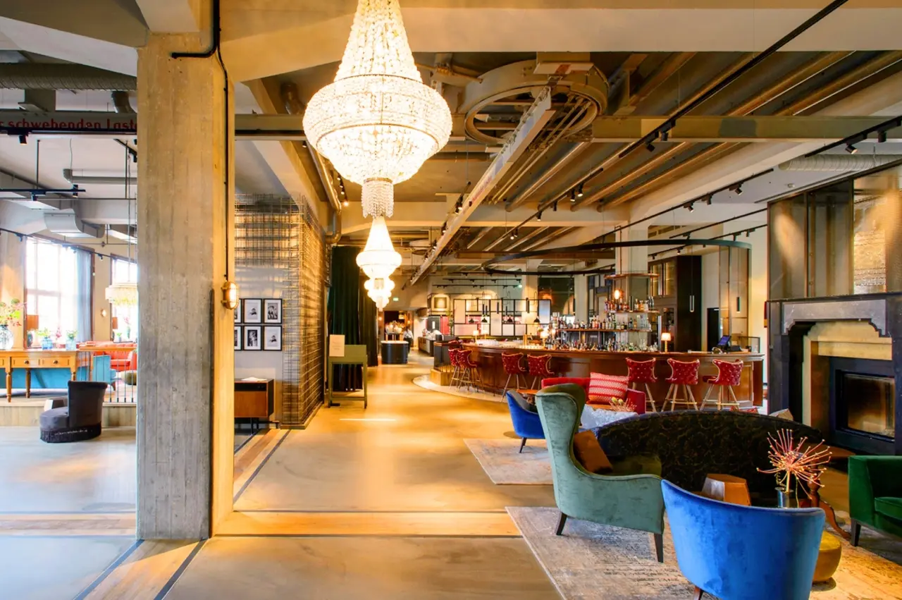 Stilvolle Lobby und Bar im Hotel Das James mit Kronleuchtern, farbigen Samtsesseln und industriellem Design.
