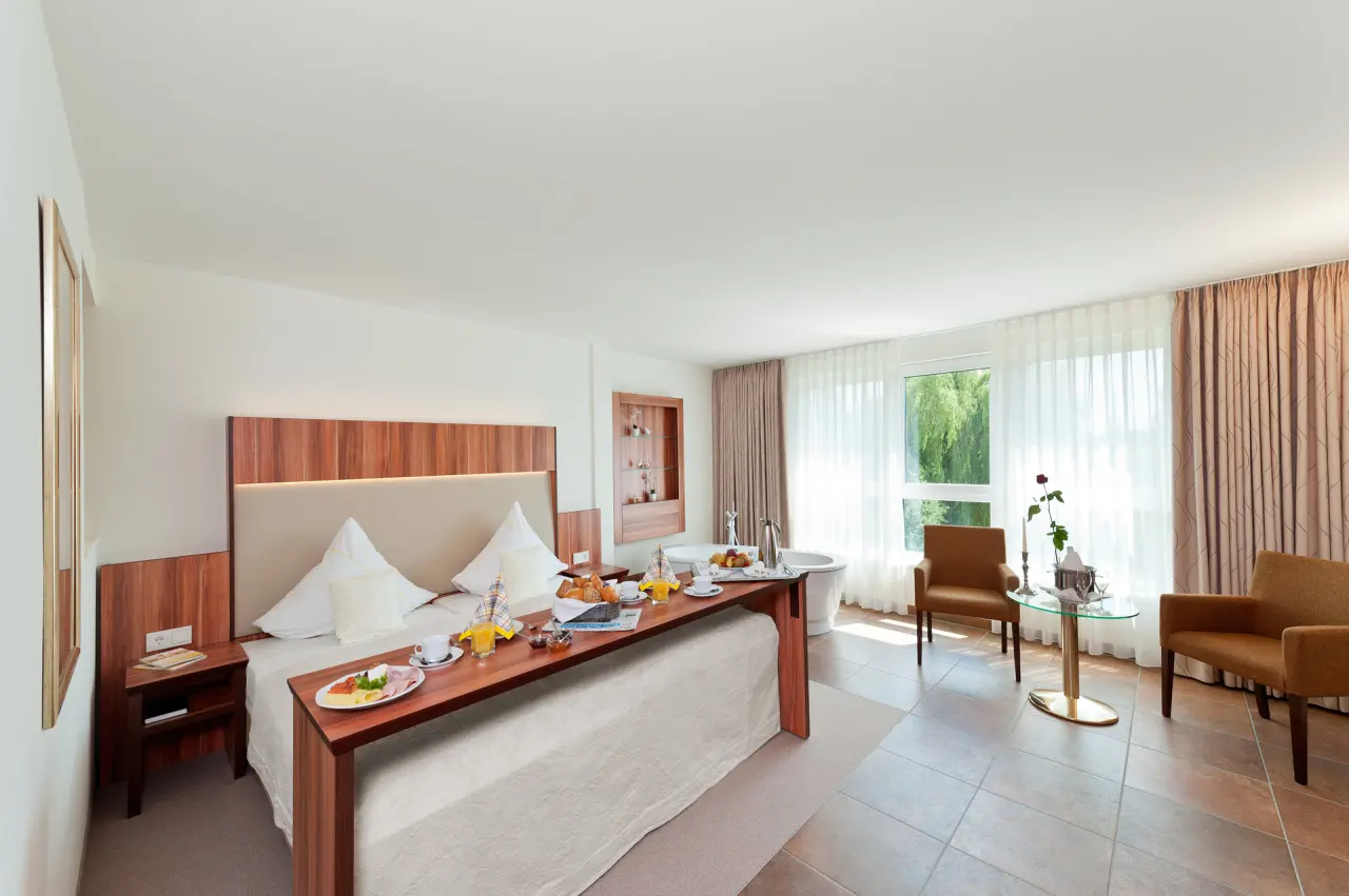 Komfortables Hotelzimmer im Ringhotel Am Stadtpark mit Frühstück im Bett und Badewanne am Fenster für entspannte Momente.