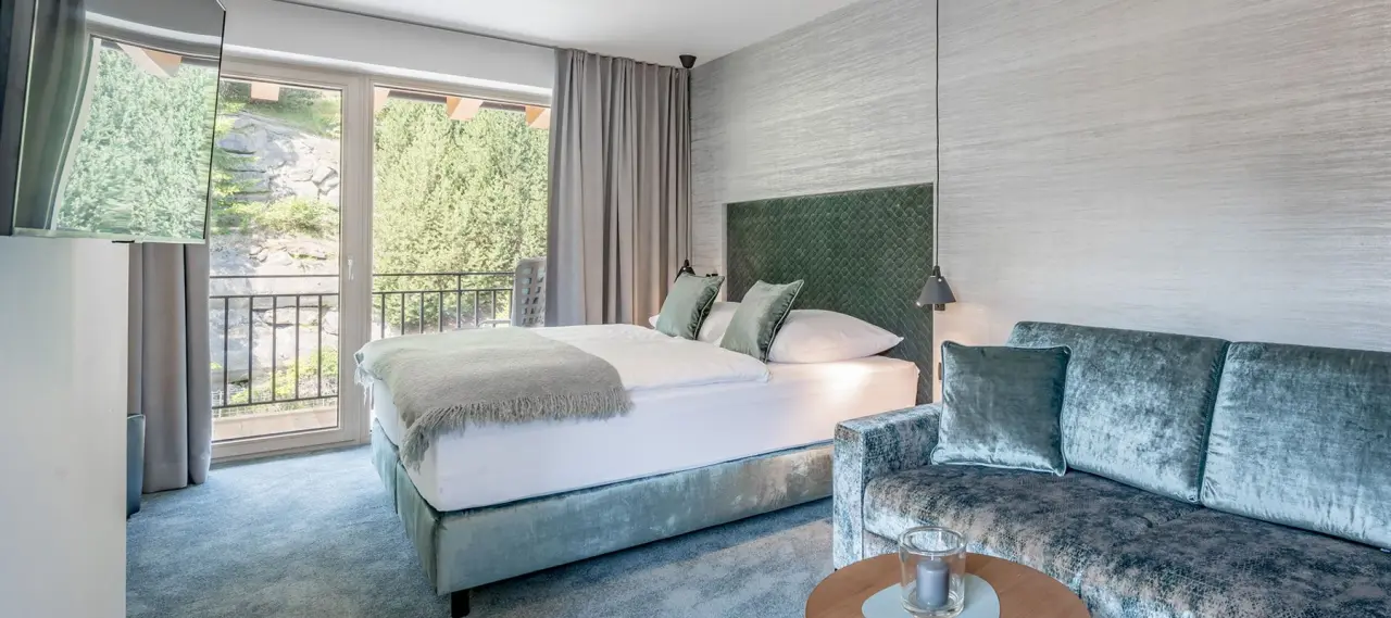 Modernes Hotelzimmer im Hotel Tyrolerhof mit Doppelbett, Sofa und Balkon mit Blick ins Grüne.