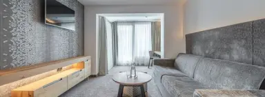 Modernes Wohnzimmer einer Suite im Hotel Tyrolerhof mit Sofa, TV und Schreibtisch am Fenster.