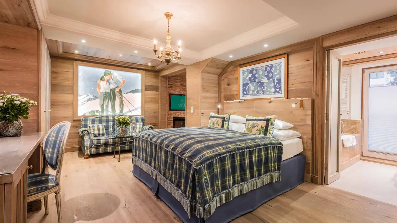 Gemütliches Doppelzimmer im Alpin Resort Sacher Seefeld mit Holzelementen, kariertem Bett und Sitzbereich.