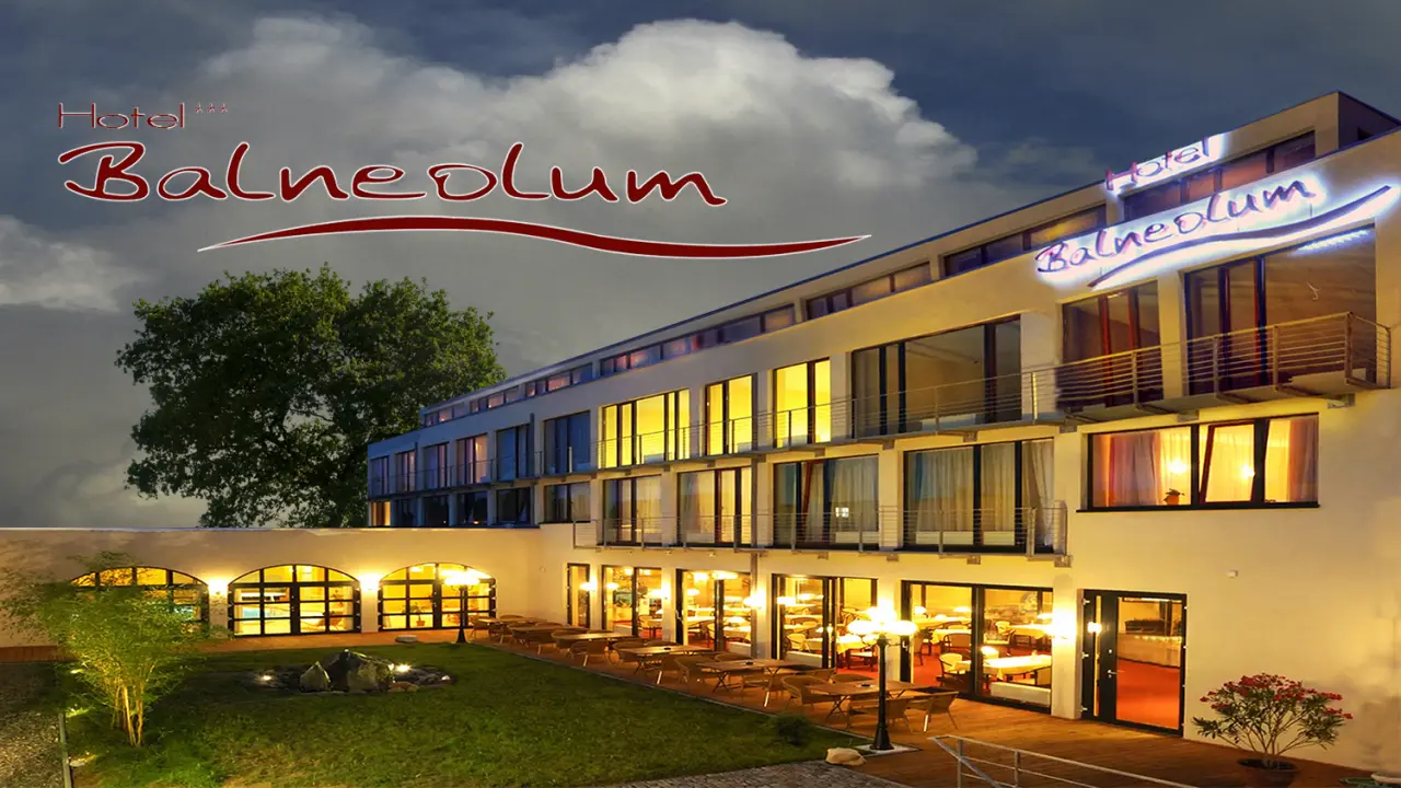 Beleuchtete Aussenansicht des Hotel Balneolum bei Abenddämmerung mit Garten und Restaurantterrasse.