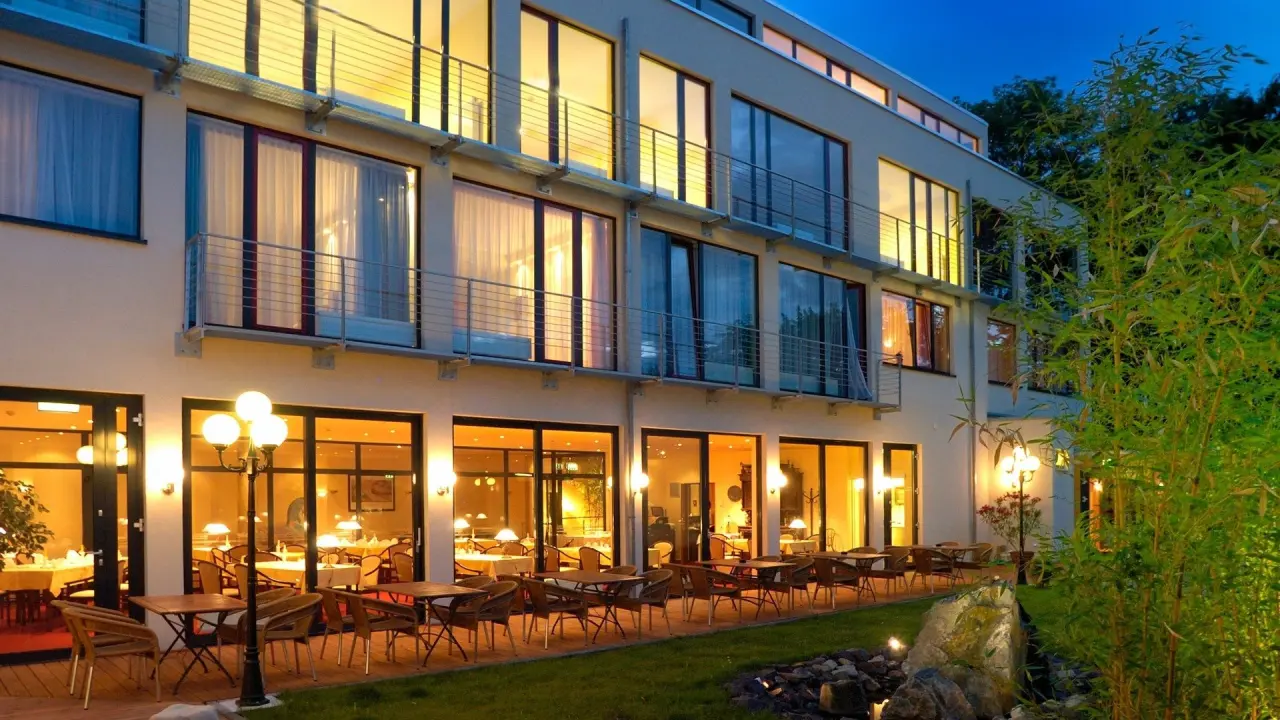 Moderne Aussenansicht des Hotel Balneolum bei Abenddämmerung mit beleuchteter Restaurant-Terrasse und Balkonen.