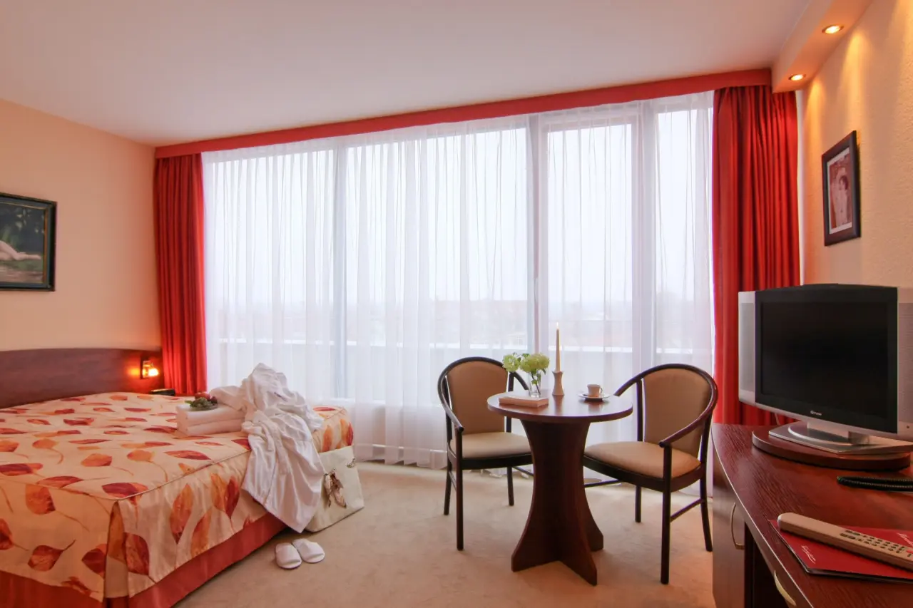 Gemütliches Hotelzimmer im Hotel Balneolum mit Doppelbett, Bademantel und Sitzbereich am Fenster.