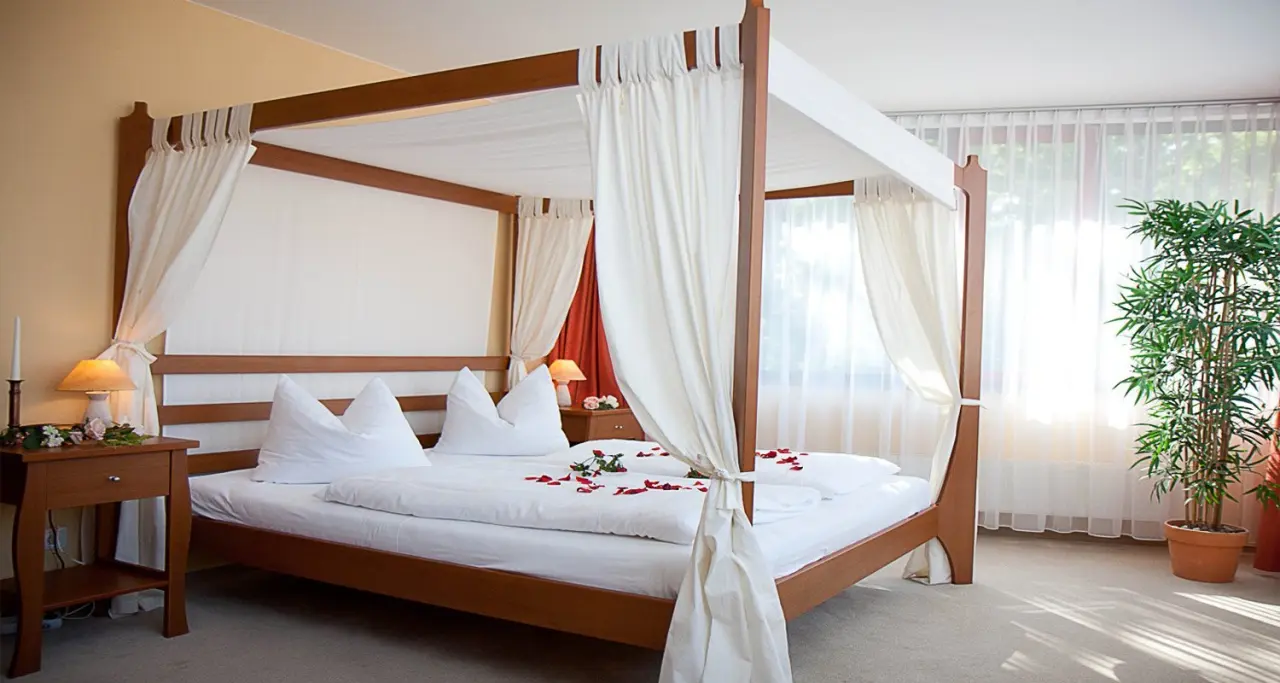Romantisches Himmelbett mit weißen Vorhängen und roten Rosenblättern in einem Hotelzimmer des Hotel Balneolum.