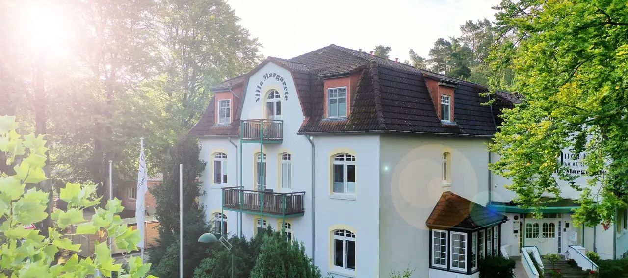 Aussenansicht des Ringhotel Villa Margarete, einer charmanten Villa umgeben von Bäumen, bei sonnigem Wetter.