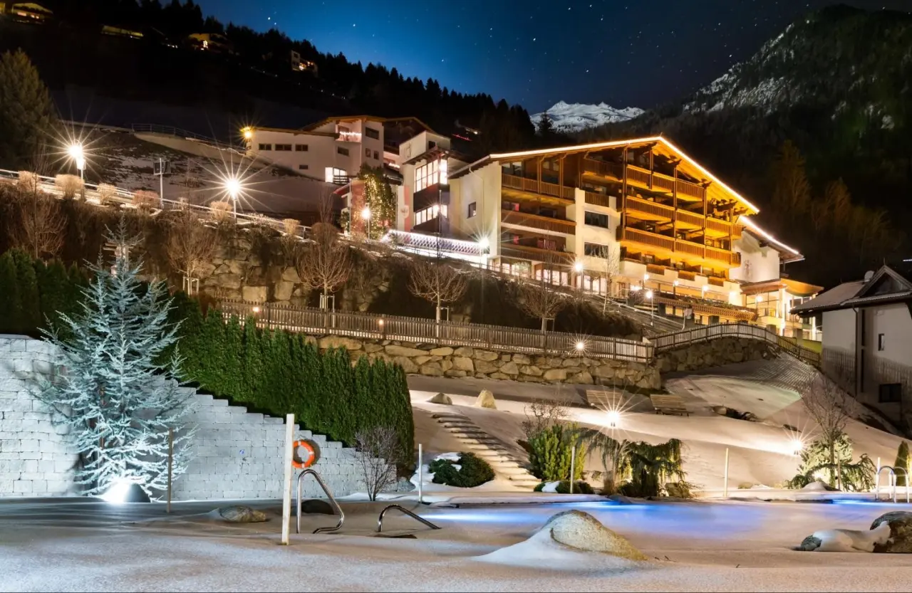 Beleuchtetes Hotel Jerzner Hof bei Nacht mit verschneitem Aussenpool und Sternenhimmel vor Bergkulisse.