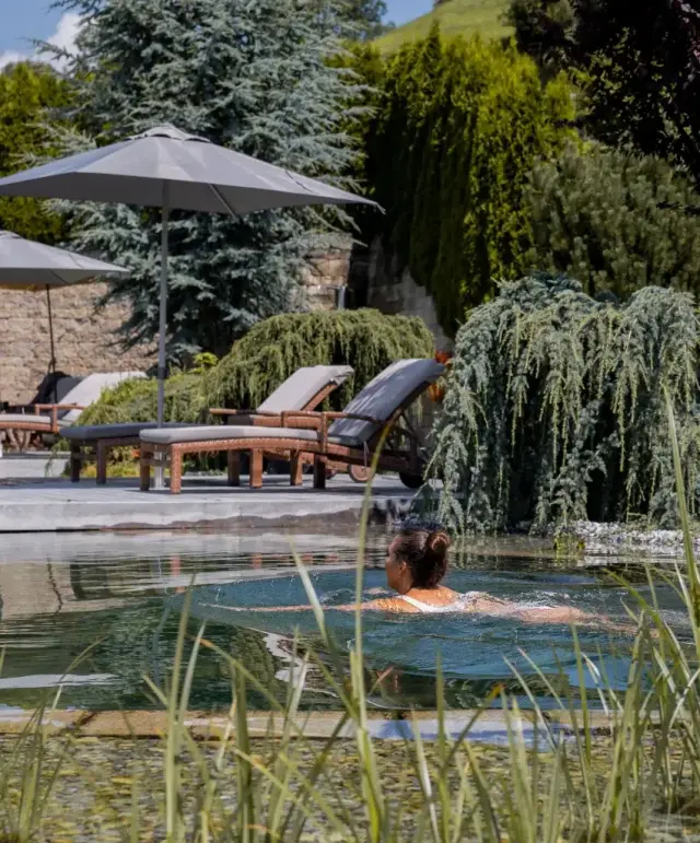Natürlicher Badeteich mit Schwimmerin und Liegestühlen im grünen Garten des Jerzner Hofs.