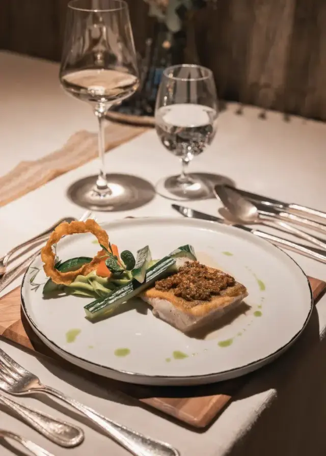 Exquisit angerichteter Fisch mit Beilagen und Wein auf einem elegant gedeckten Tisch im Restaurant des Jerzner Hof.