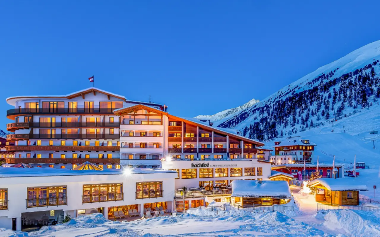 Alpen-Wellness Resort Hochfirst bei Dämmerung im Winter, umgeben von verschneiten Bergen und Pisten.