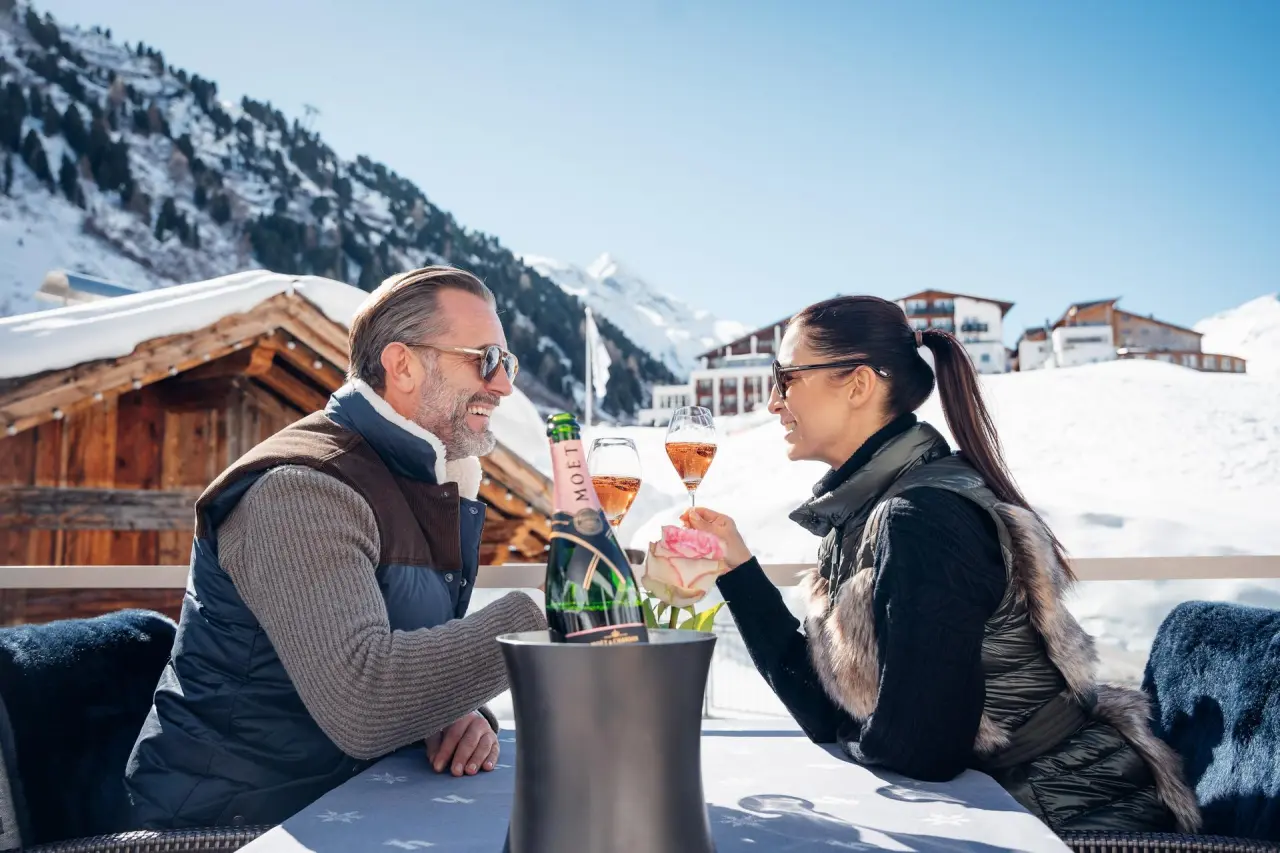 Alpen-Wellness Resort Hochfirst in Obergurgl – Paar genießt Champagner auf sonniger Winterterrasse | Wellnesshotel Tirol