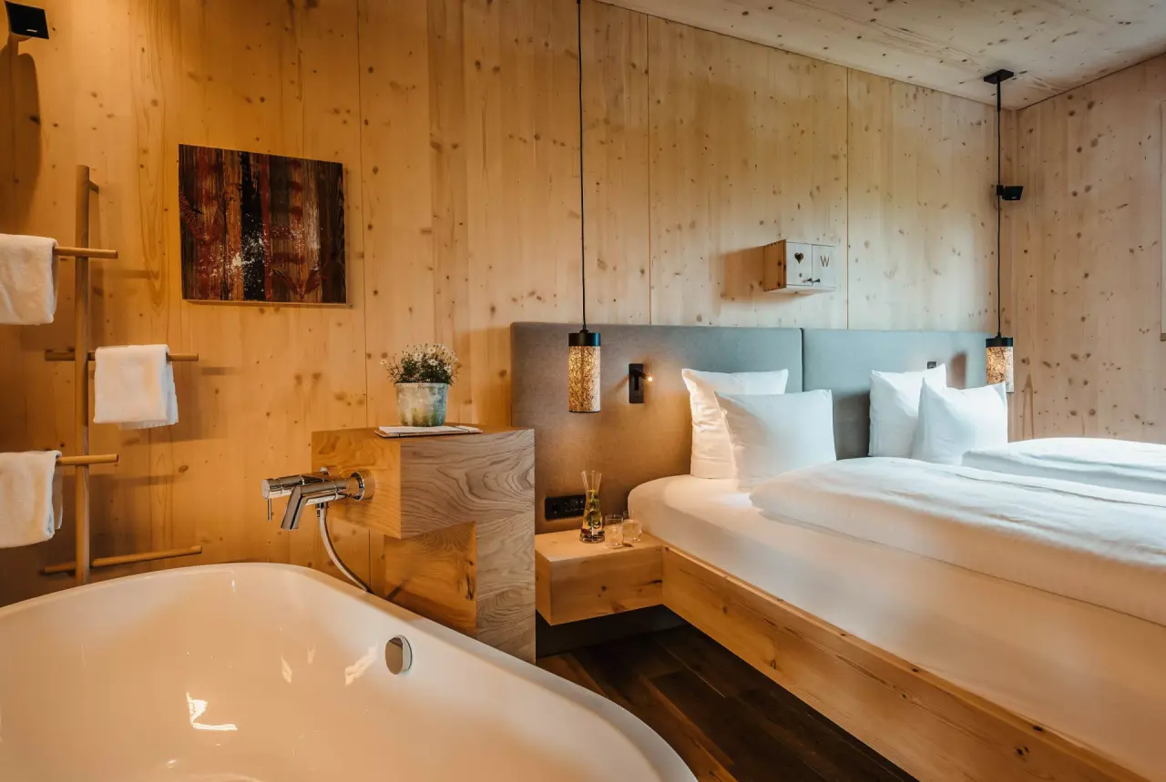 Gemütliches Hotelzimmer im WERDENFELSEREI mit Holzwänden, Doppelbett und freistehender Badewanne für entspannte Momente.