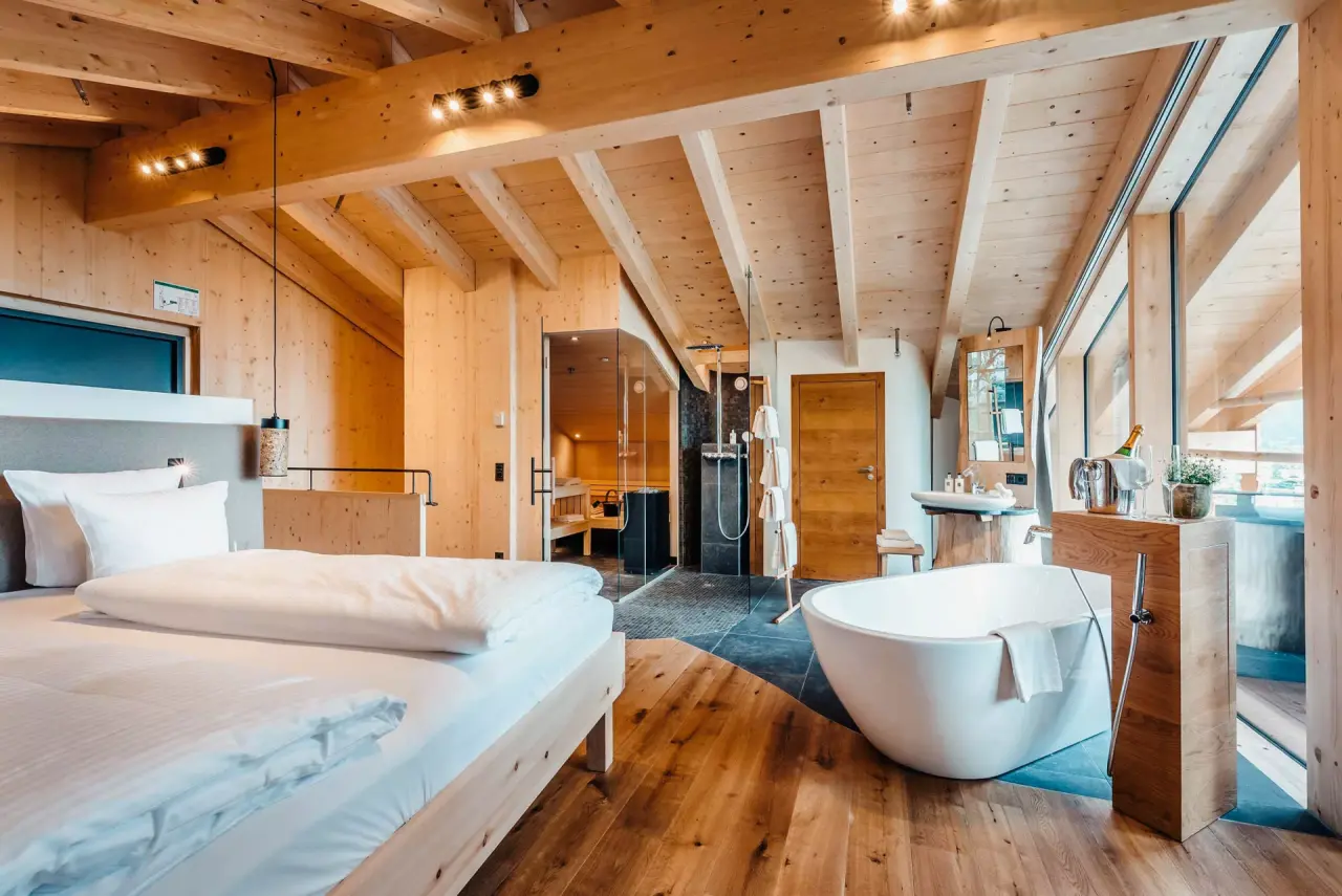 Luxuriöses Hotelzimmer der WERDENFELSEREI mit privater Sauna, freistehender Badewanne und Holzakzenten für entspannte Momente.