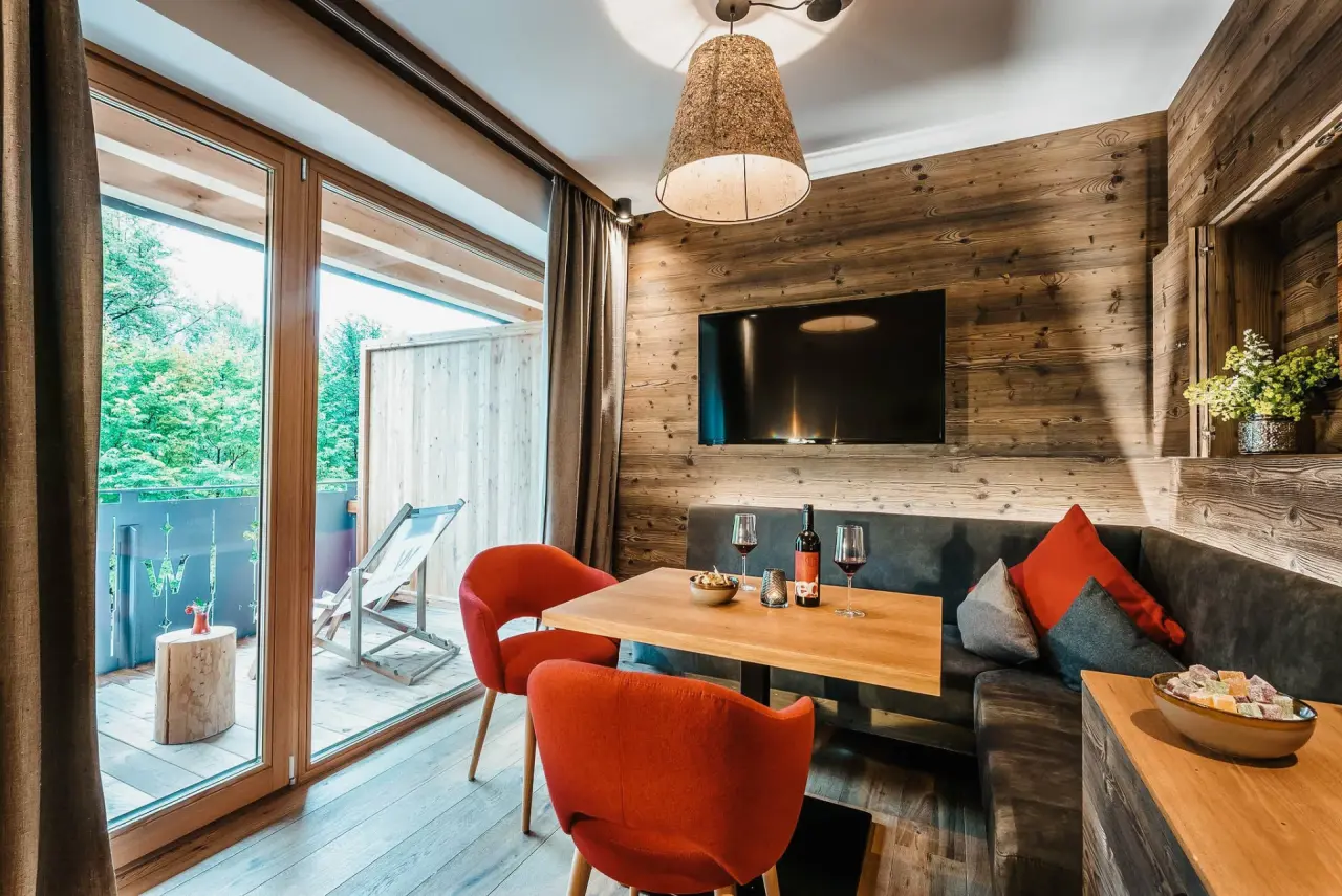 Gemütliches Hotelzimmer der WERDENFELSEREI mit Holzeinrichtung, Essbereich, TV und Balkon mit Blick ins Grüne.