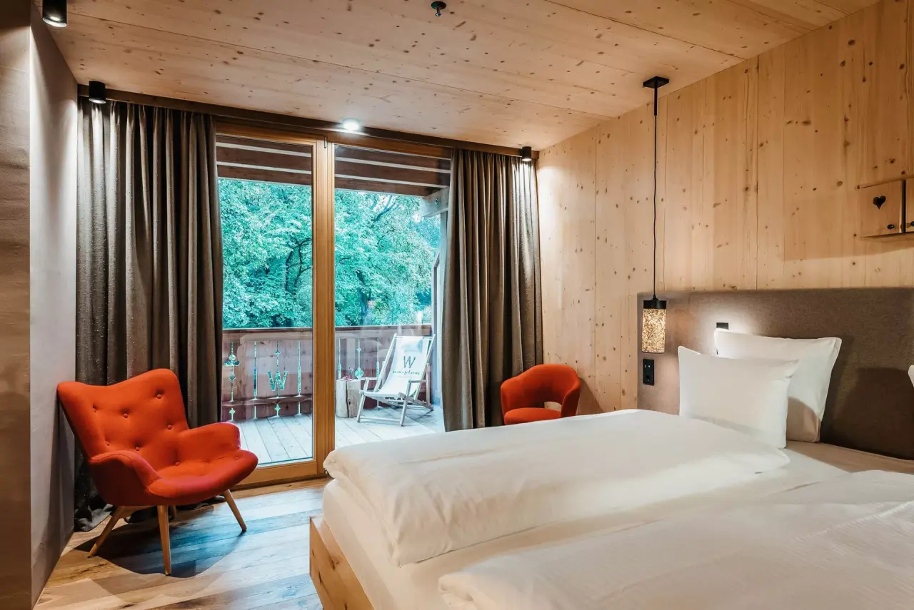 Gemütliches Hotelzimmer der WERDENFELSEREI mit Holzelementen, bequemen Betten und Balkonblick ins Grüne.