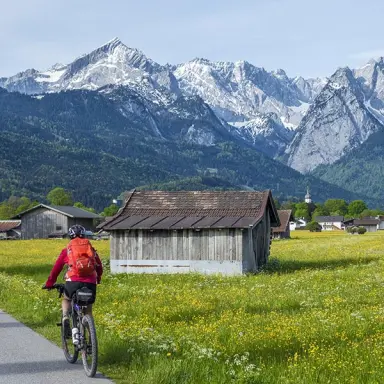 Radfahrerin auf einem Feldweg mit Blick auf die majestätische Zugspitze und Alpenlandschaft nahe Hotel Zugspitze.