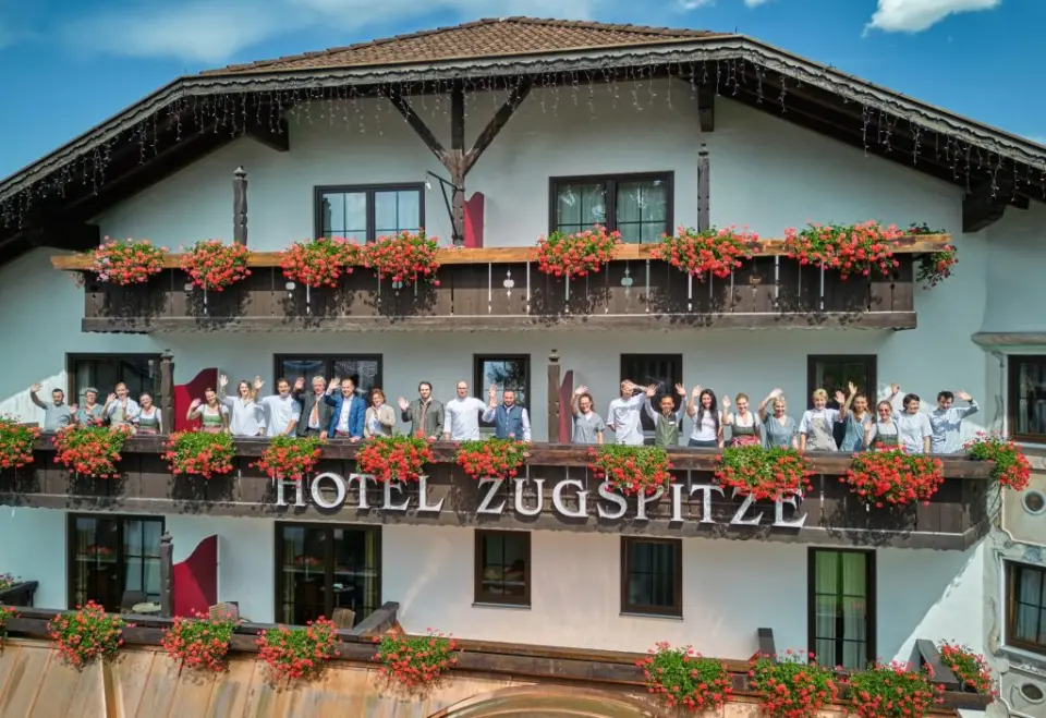 Aussenansicht des Hotel Zugspitze mit traditioneller Architektur, blühenden Balkonen und dem freundlichen Hotelteam.