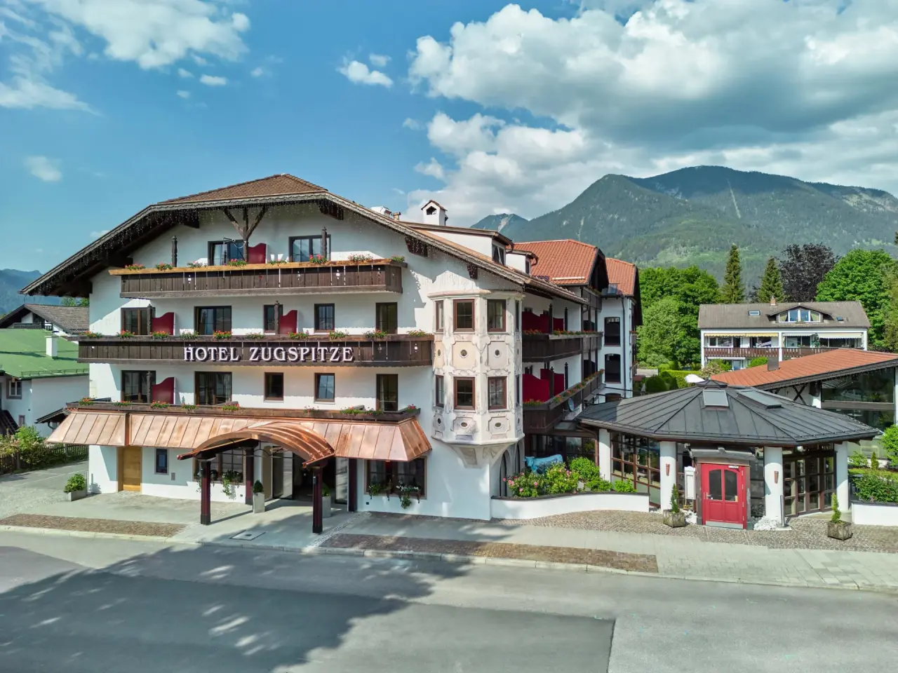 Traditionelle Aussenansicht des Hotel Zugspitze in Garmisch-Partenkirchen mit Alpenpanorama und blauem Himmel.