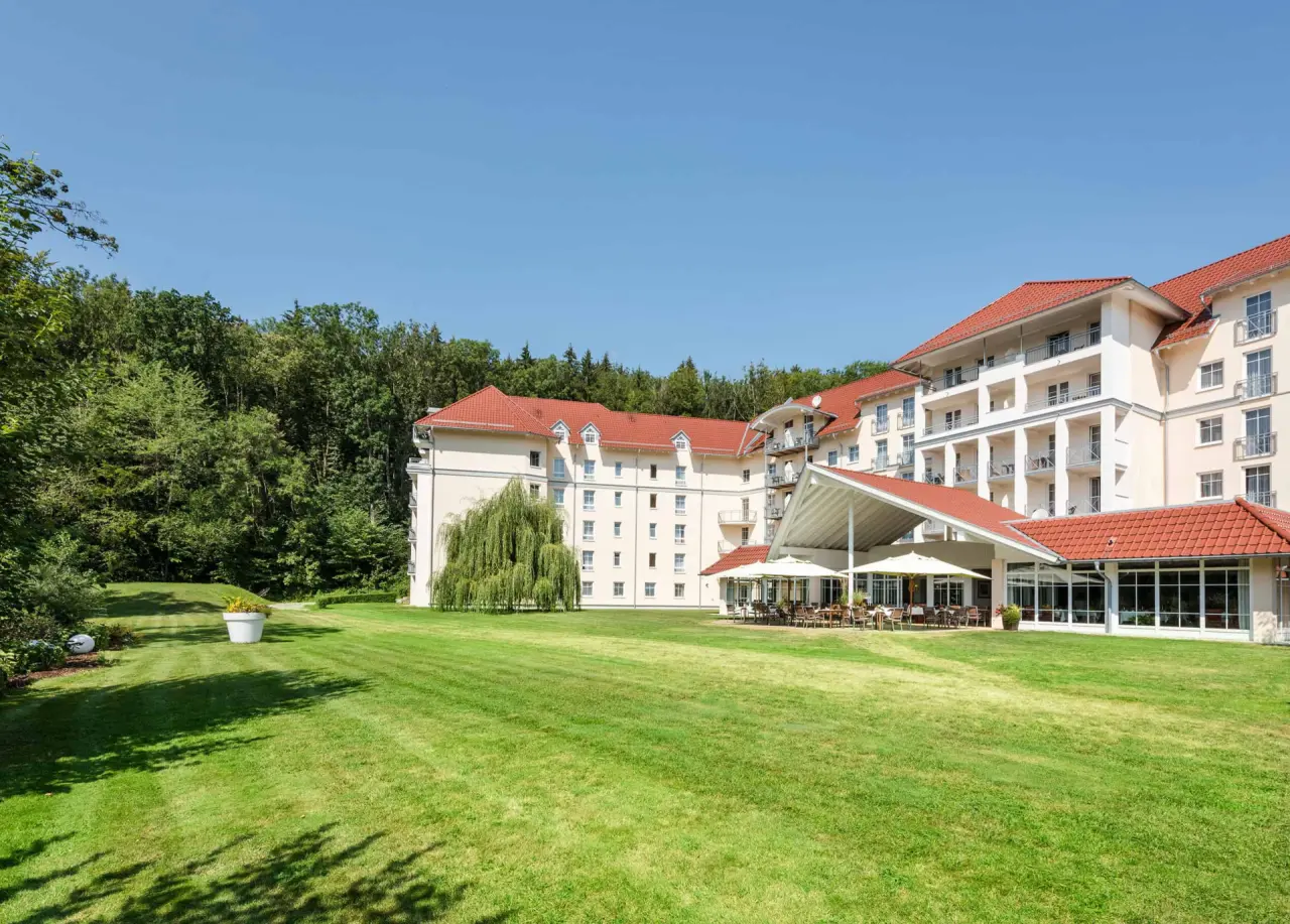 Aussenansicht des Best Western Plus Parkhotel Maximilian mit grosser Rasenfläche, Wald und Sonnenterrasse.